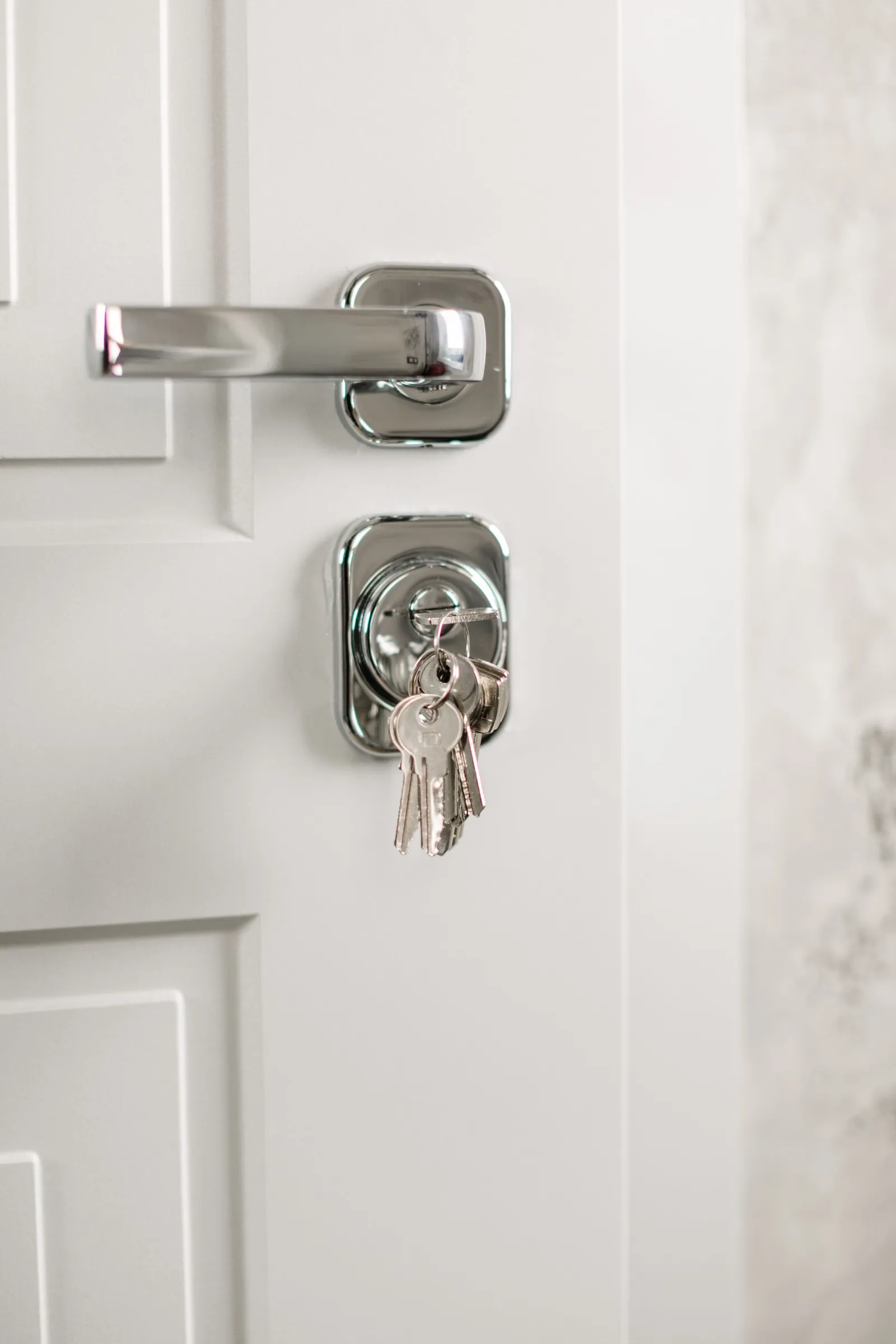 Close-up of a silver door handle and deadbolt with house keys hanging in the lock